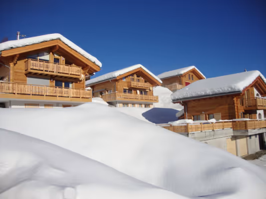 Holzhäuser mit Schneebedeckung unter klarem blauem Himmel an einem sonnigen Wintertag.