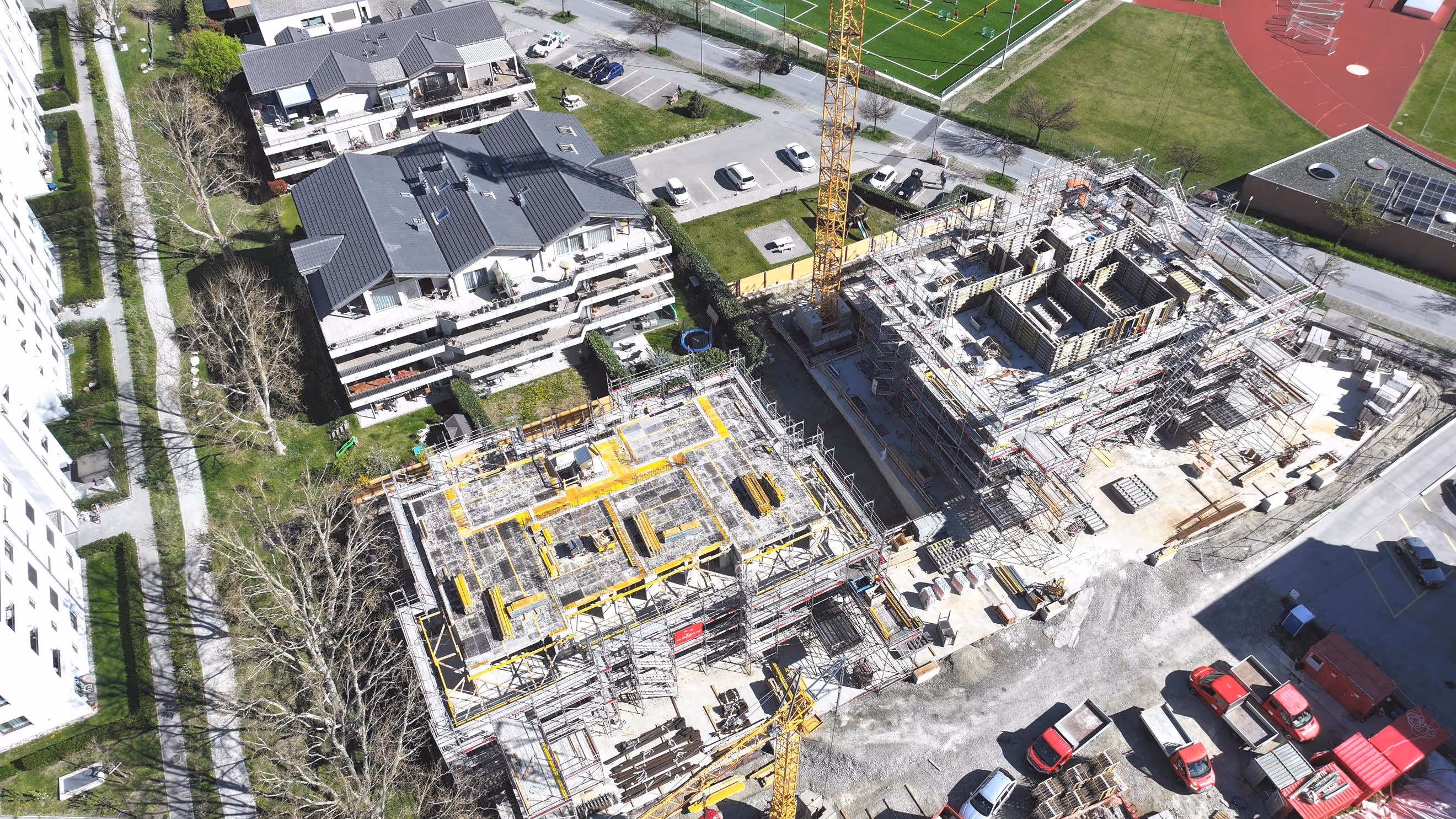 Luftaufnahme von zwei Gebäuden im Bau neben bewohnten Häusern und Parkplätzen.