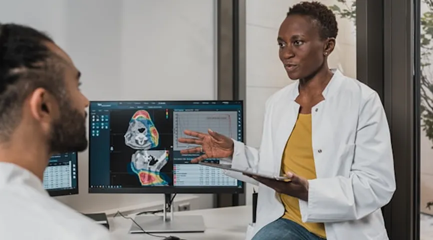 Female doctor explaining medical scan images on a monitor to a male patient in a consultation room.