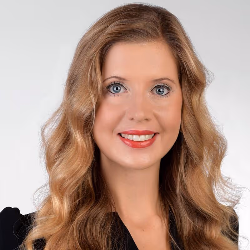 Professional headshot of Nathalie Redmo smiling with long blonde hair and blue eyes against a grey background