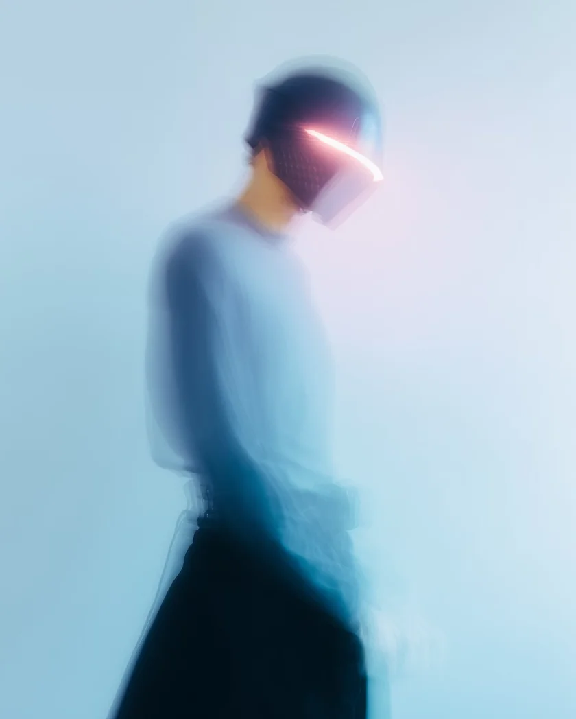 Blurred figure wearing a glowing visor helmet against a light blue background.