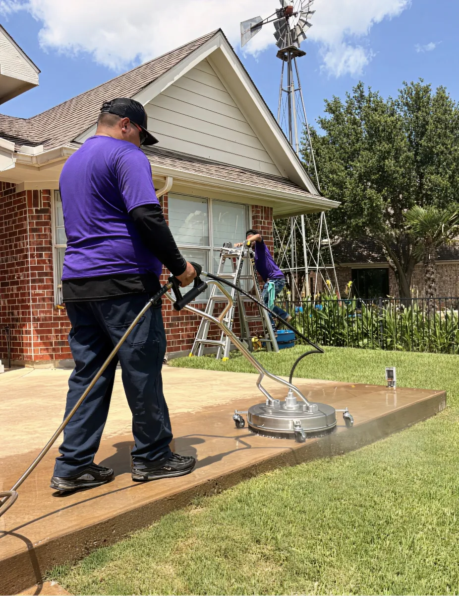 Technician pressure washing a concrete walkway at a Dallas home