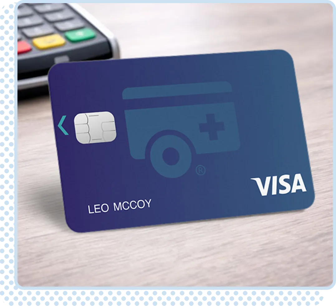 Blue Visa credit card with chip and medical cross logo placed on a wooden surface near a payment terminal.