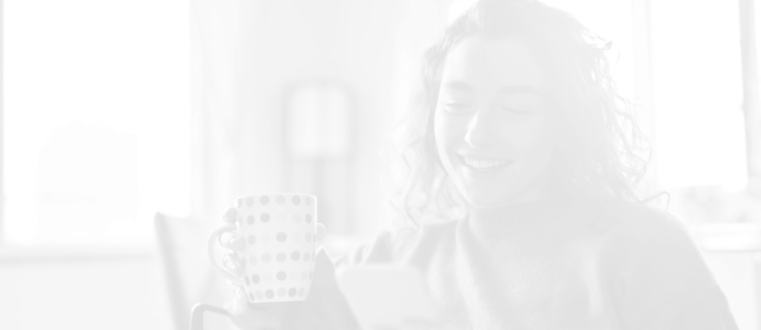 Smiling woman with curly hair holding a polka-dotted mug and looking at her smartphone indoors.