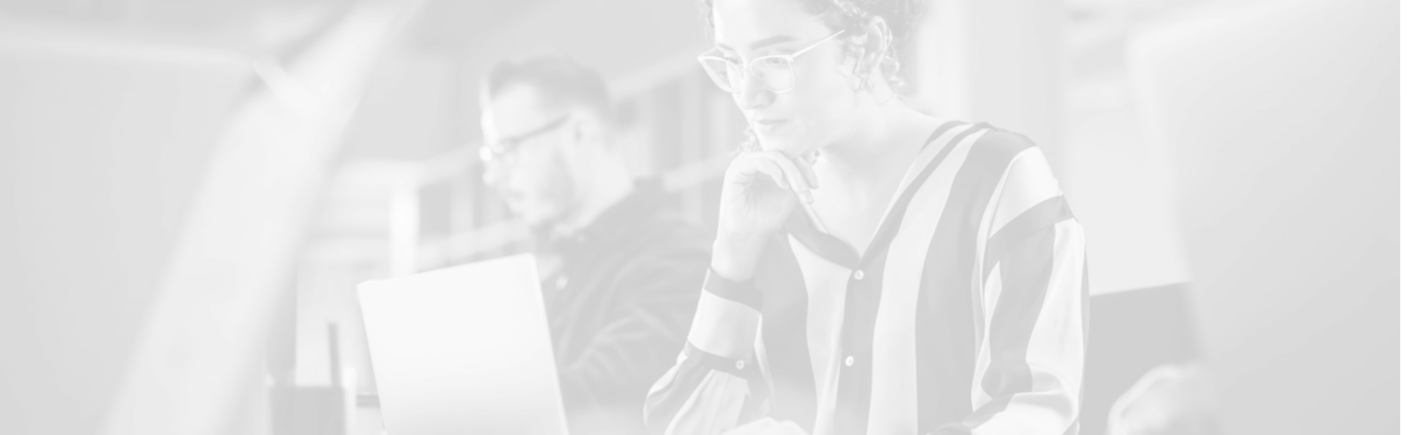 Two focused people working on laptops in a modern office space.