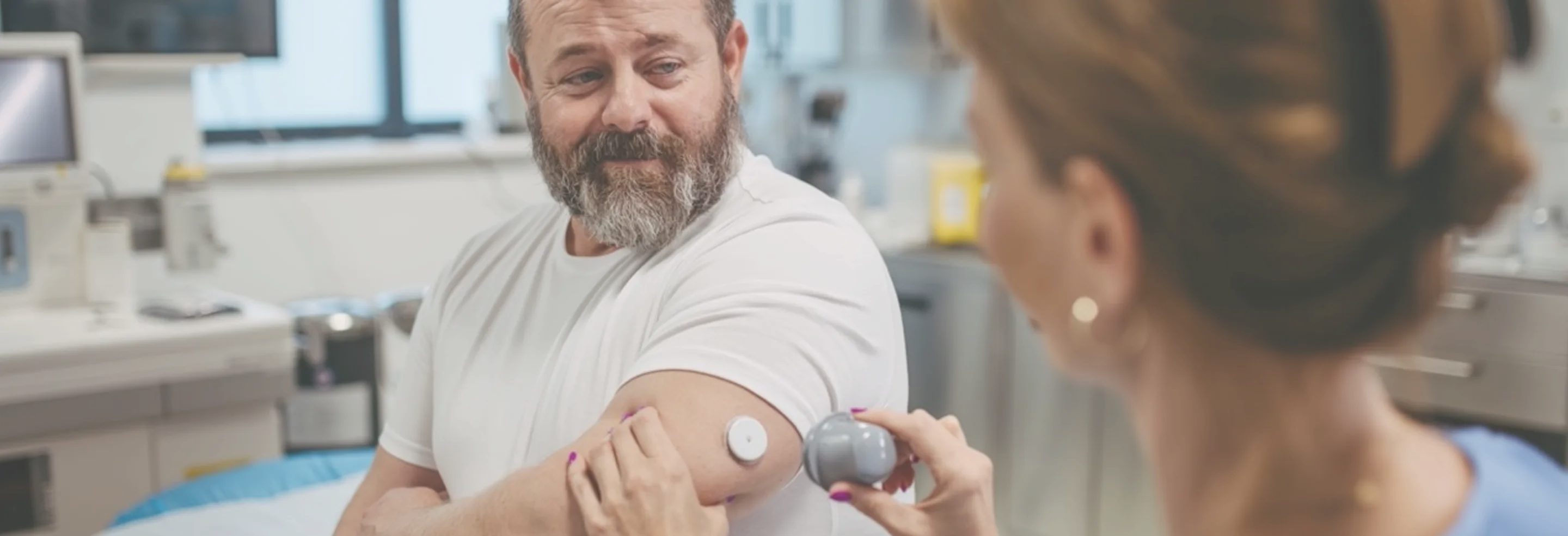 Healthcare professional placing a medical sensor on a man's upper arm in a clinical setting.