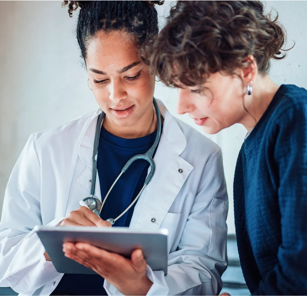Female doctor with stethoscope showing information on a tablet to a woman patient.