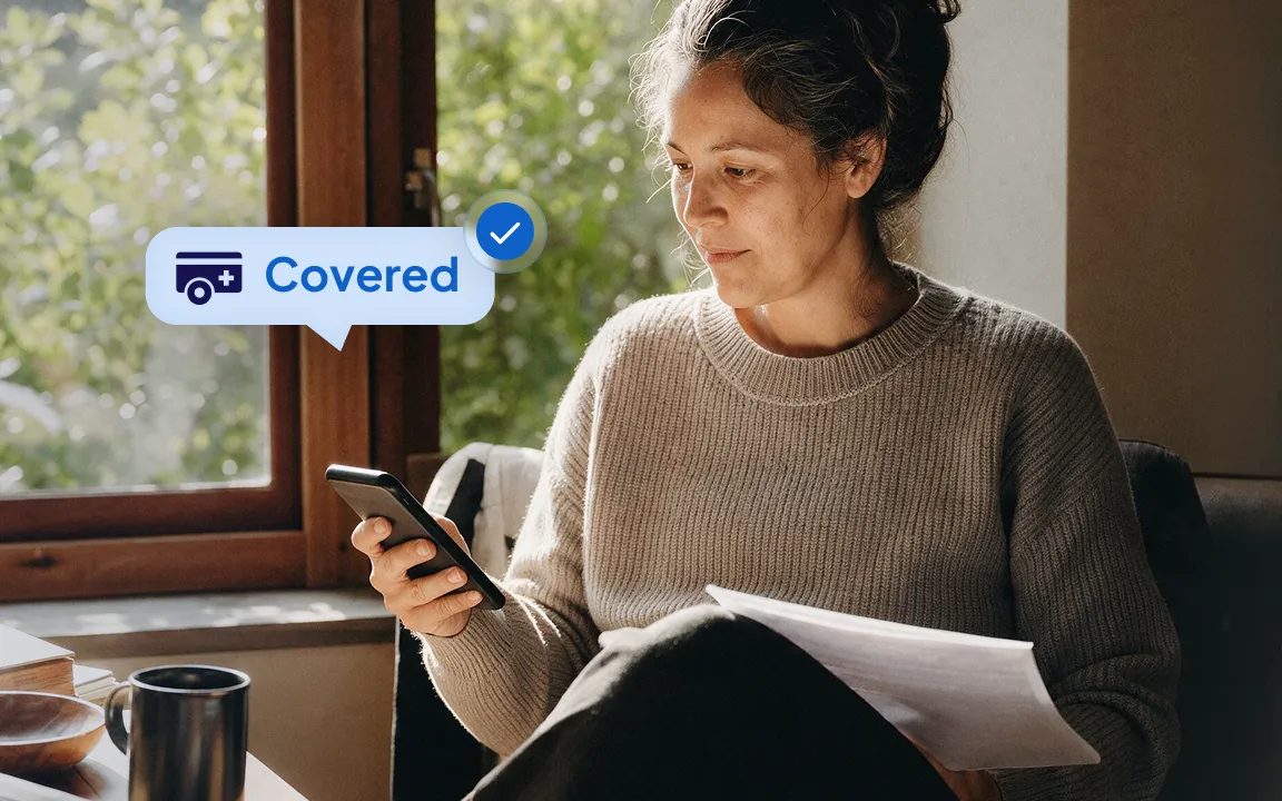 Woman reading on her phone at home, with a Sidecar Health badge showing Covered.