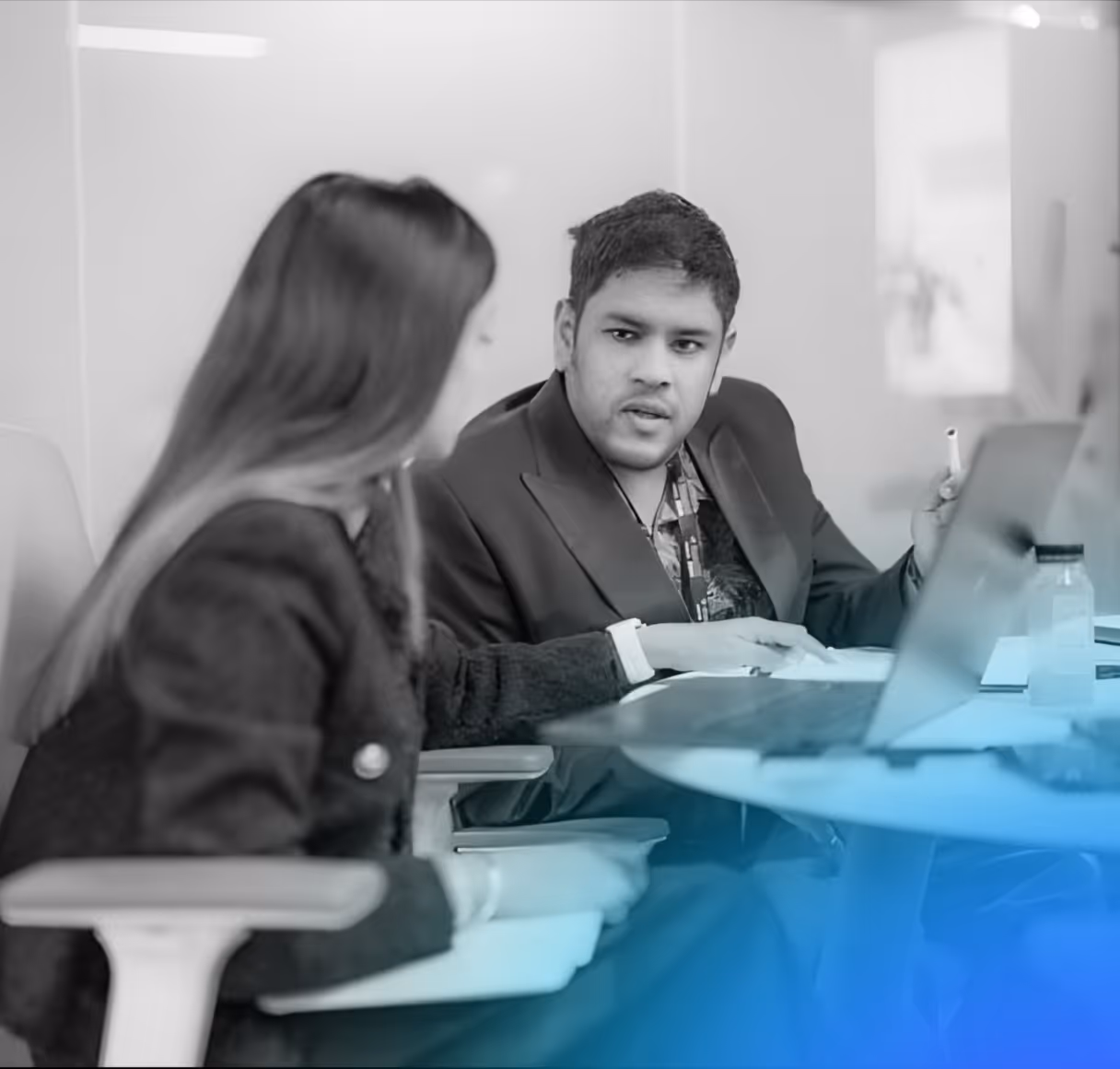 Man and woman in a discussion at a round table with a laptop and notebook in an office setting.