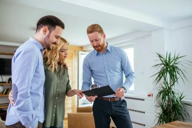 Real estate agent showing a clipboard to a couple inside a modern living room.