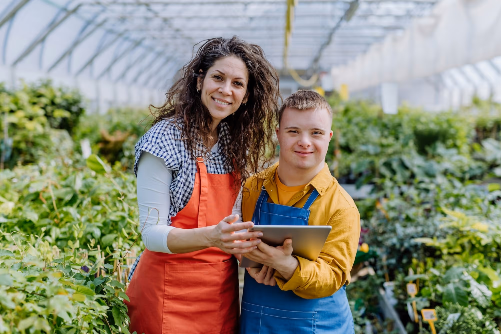A woman and young man using Equip technology in a greenhouse surrounded by rows of plants.