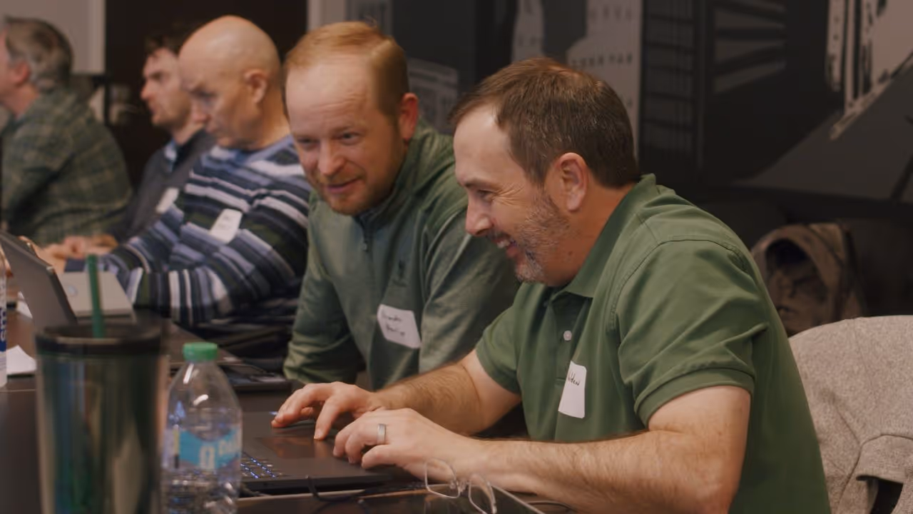 Participants smiling and working on laptops during a Caravan training session.