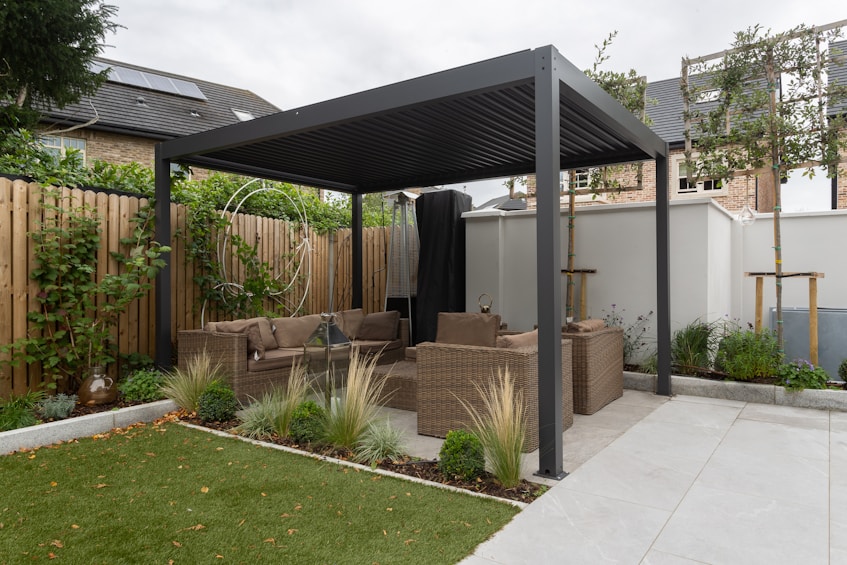 Outdoor patio seating area under a modern pergola with wicker sofas and green lawn nearby.