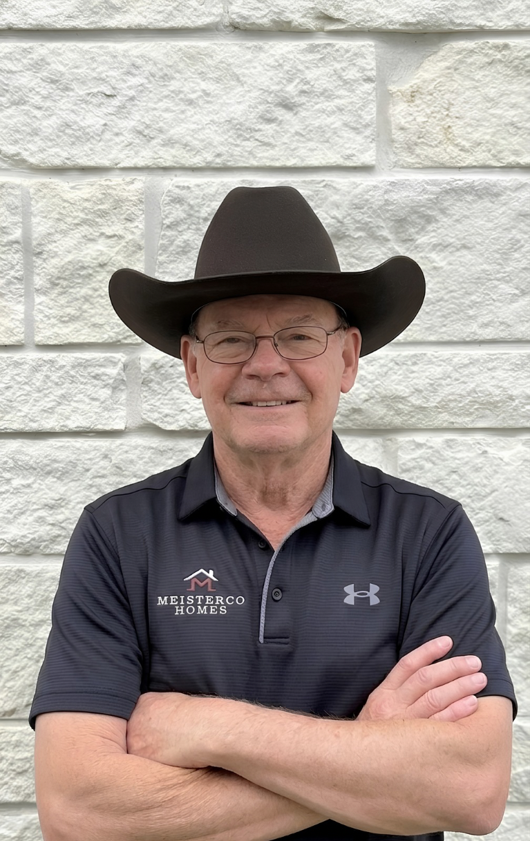 Smiling man wearing glasses, a black cowboy hat, and a Meisterco Homes polo with arms crossed.