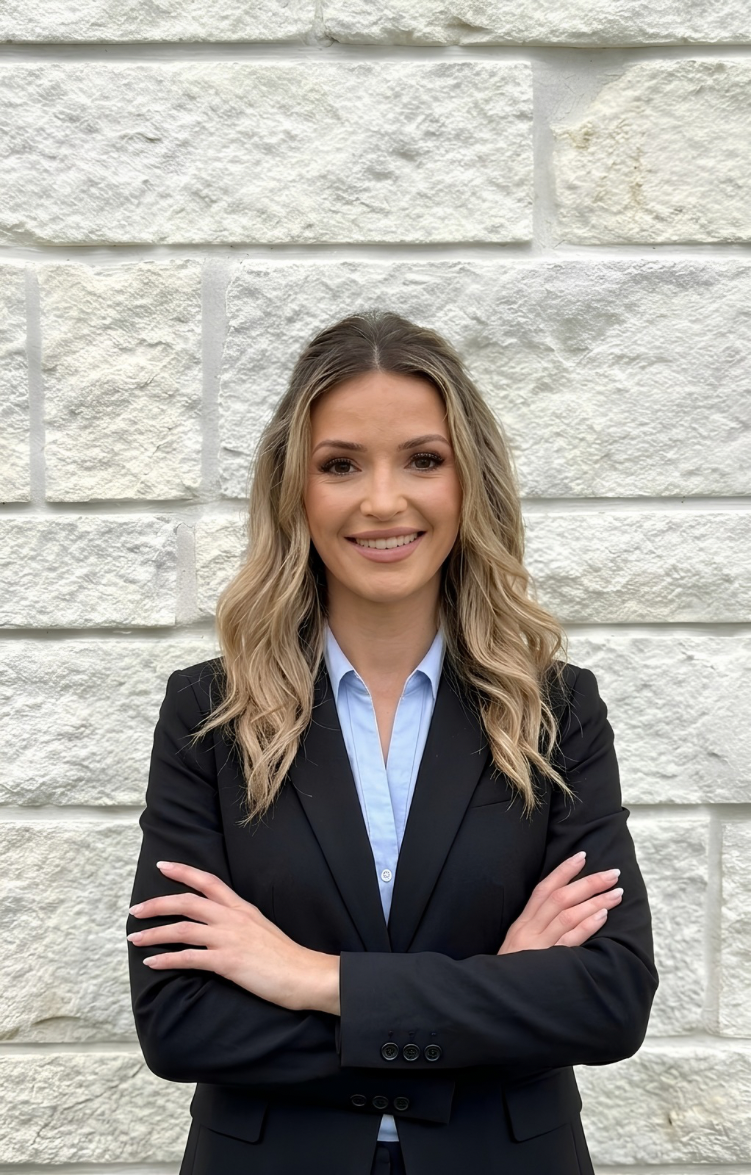 Smiling woman with wavy hair in a black blazer and light blue shirt standing with arms crossed.