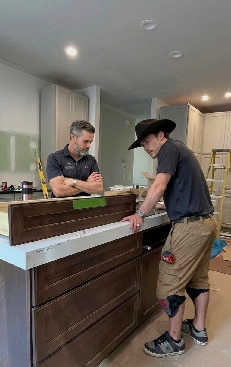 Two men examining wooden kitchen cabinet doors on a marble countertop in a home under renovation.