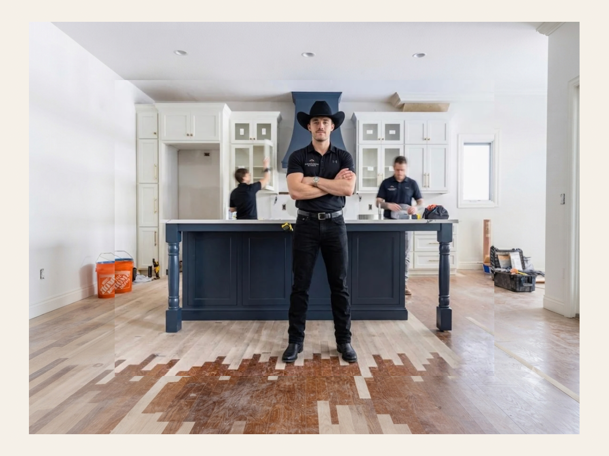Man in black cowboy hat and clothes stands in front of a kitchen island with workers installing cabinets.