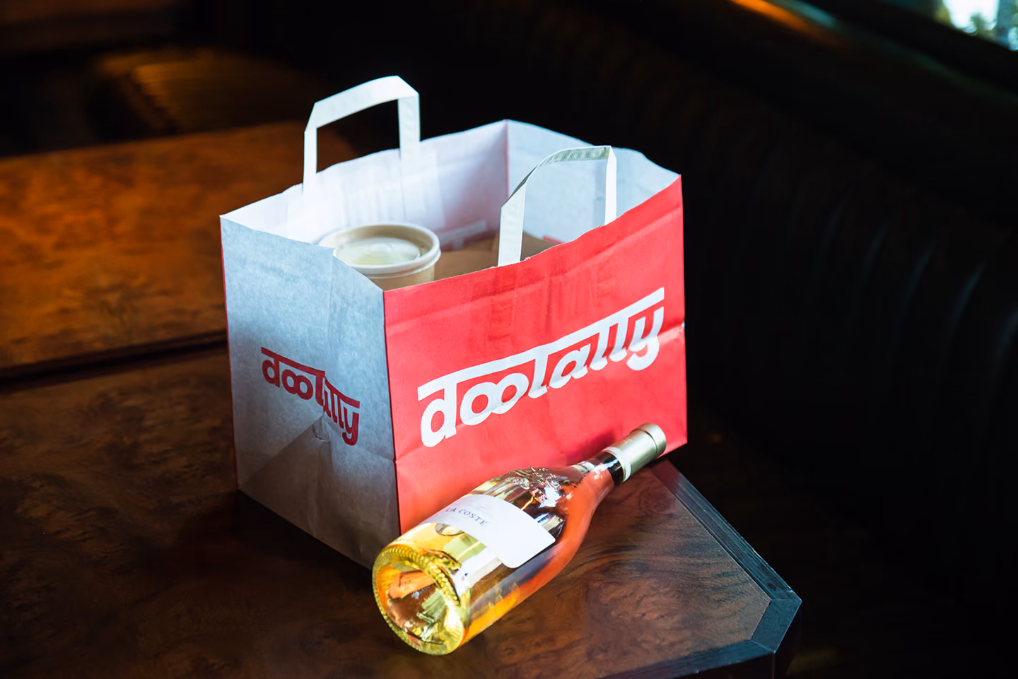 Red "dotally" branded tote bag and bottle placed on a wooden bar counter