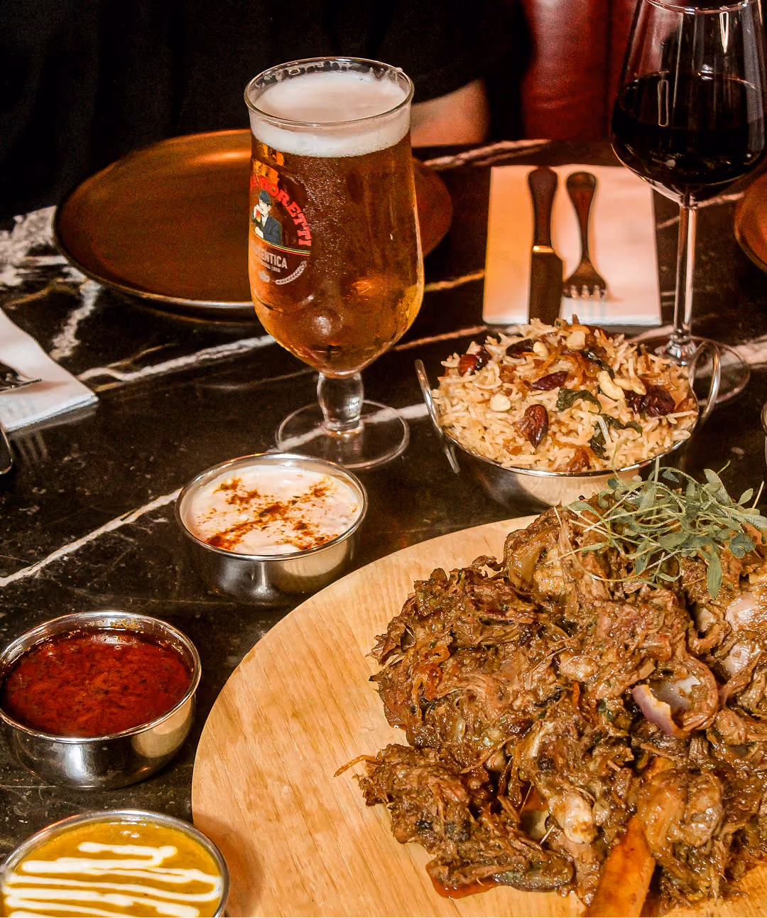 Slow-roasted Sikandari raan on a wooden board with pulao, sauces and a pint of beer at Doolally Dublin