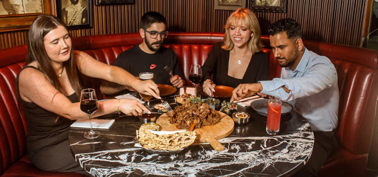 Four friends sharing the Diwali Raan in a red leather booth at Doolally, Dublin 2