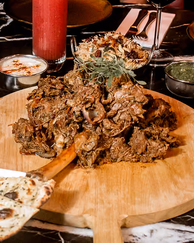 Fall-off-the-bone Sikandari raan served on a wooden board with pulao and garlic naan