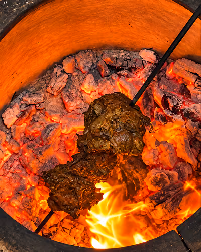 Lamb roasting over glowing charcoal in a tandoor