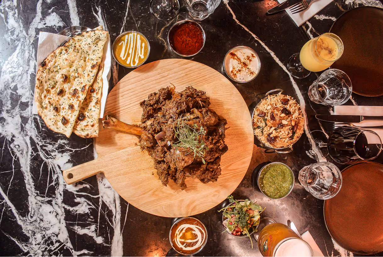 Overhead view of the Diwali Raan, a whole roast leg of lamb served with eight sides including garlic naan, pulao and chutneys