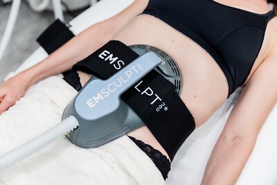 Person receiving EMSculpt body contouring treatment with a device strapped to the abdomen.