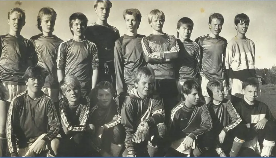 Sort-hvitt gruppebilde av 17 unge fotballspillere i treningsdrakter utendørs.