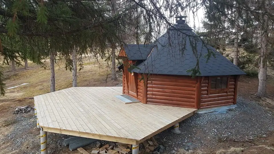 Trekantet treplattform med lite tømmerhytte i skogsområde.