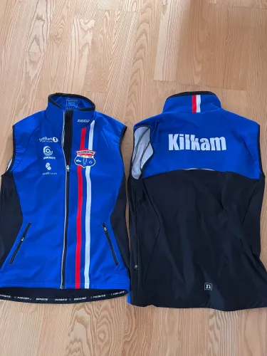 To blå og svarte sportsvester med logoer og tekst utslått på tregulv, front- og bakside synlig.