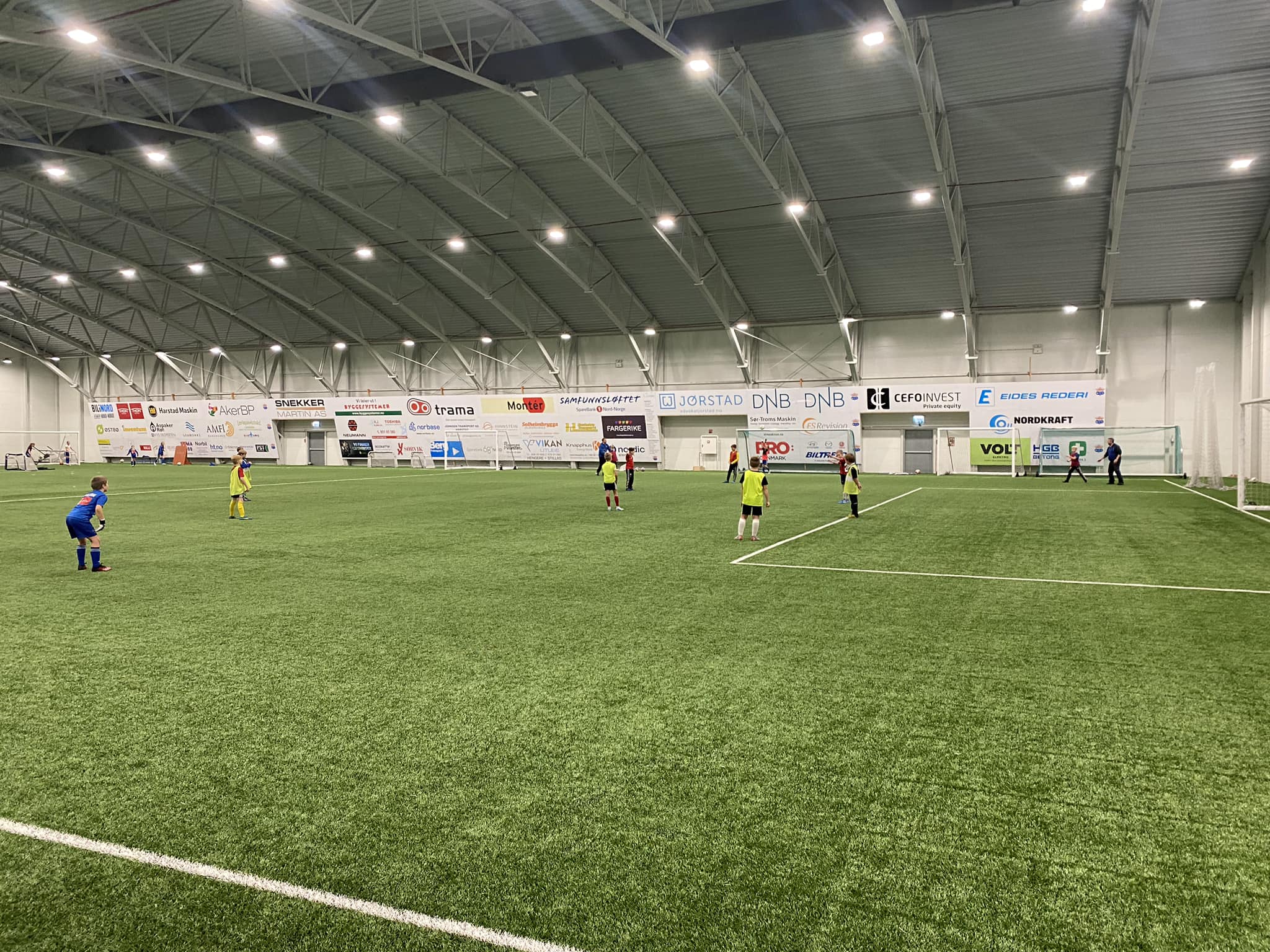 Innendørs kunstgressbane med barn som spiller fotball iført røde og gule drakter.