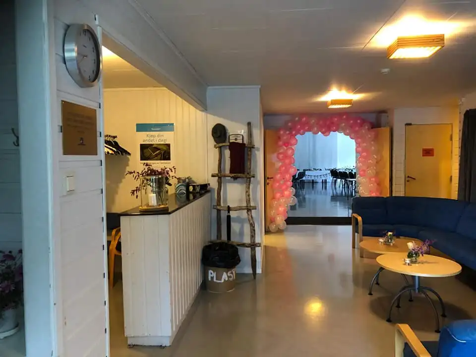 Inngangsparti med rosa ballongbue som fører til et rom med bord og stoler, blå sofa og små bord i forgrunnen.