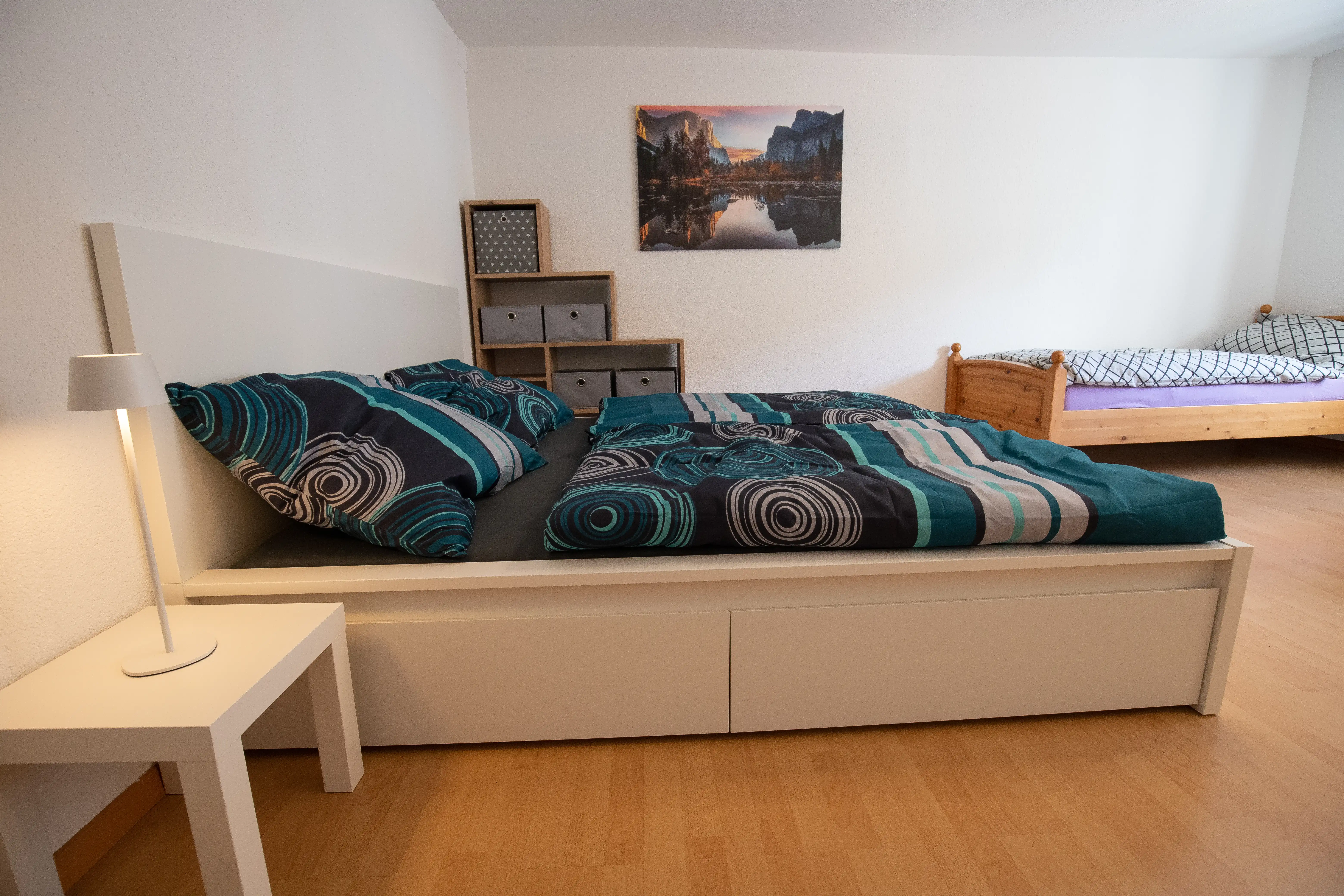 Gemütliches Doppelzimmer mit modernem Bett, Nachttischlampe und zusätzlichem Einzelbett im Hintergrund