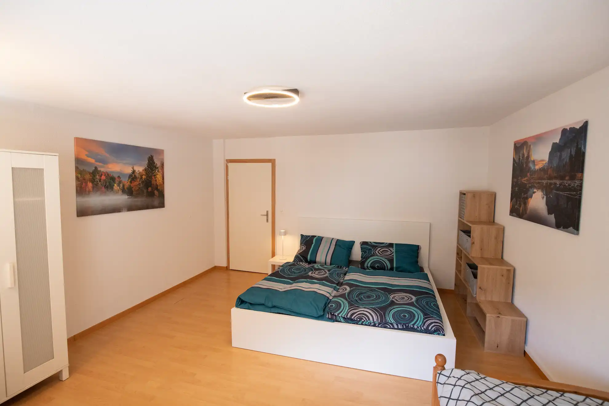 Schlicht eingerichtetes Schlafzimmer mit Doppelbett, Holzregal und zwei Naturfotografien an den Wänden.