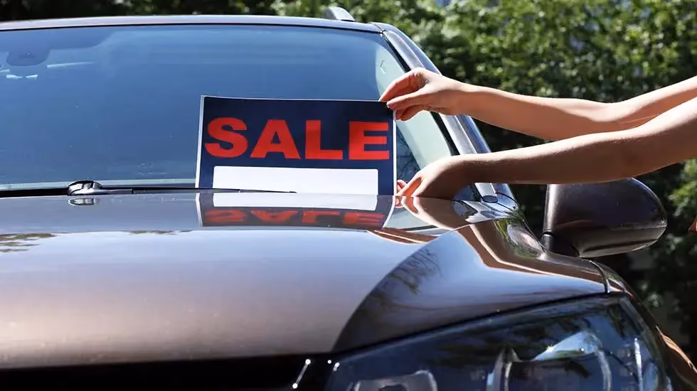 Person placing a sale sign on a car, representing selling a vehicle in NZ.