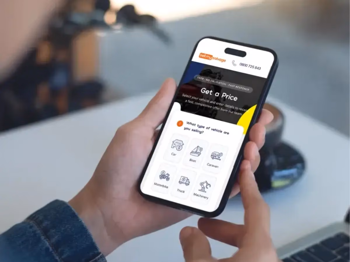 A person holding a mobile phone displaying the 'sell my salvage' website page with options to select different vehicle types.