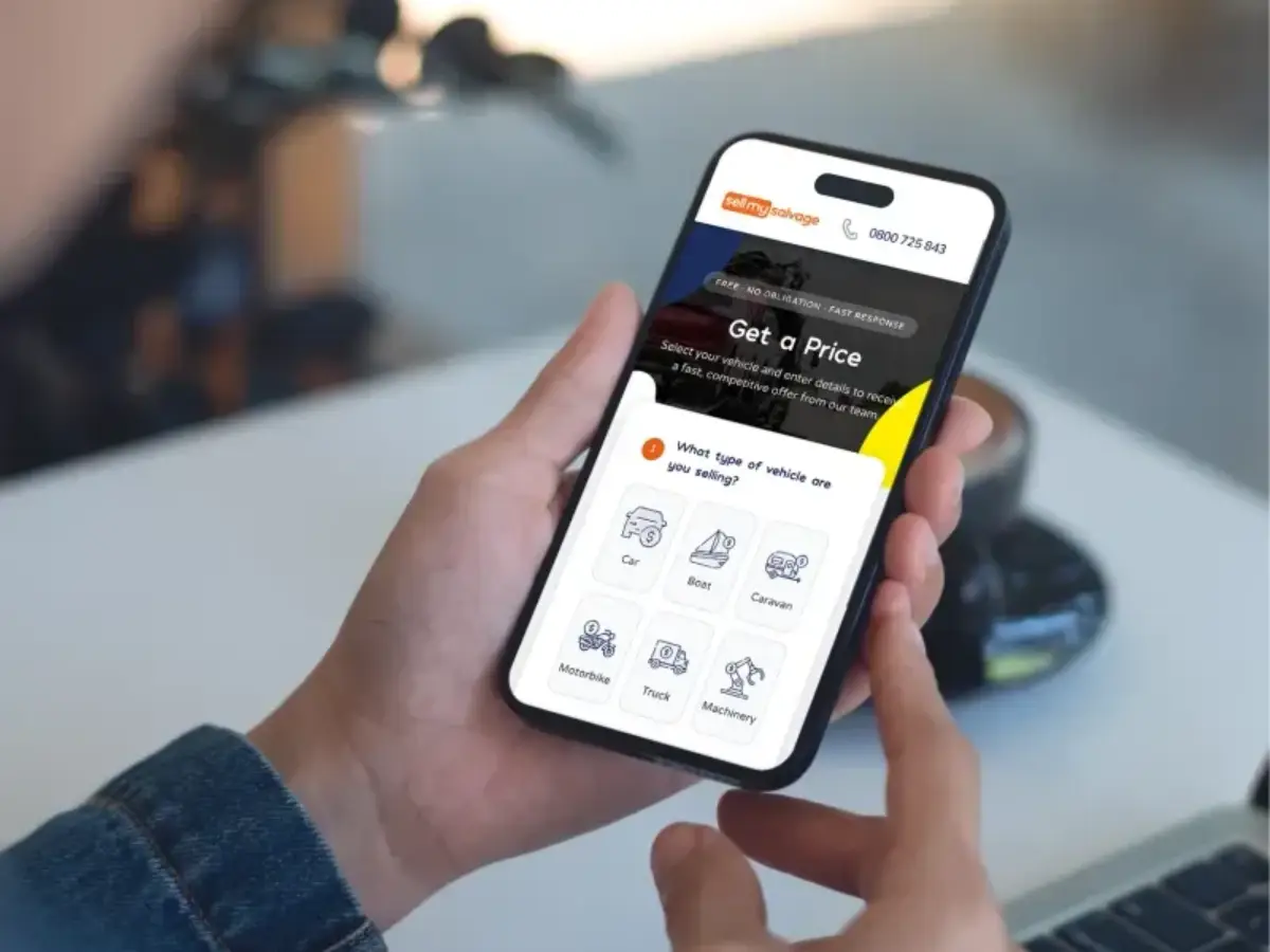 A person holding a mobile phone displaying the 'sell my salvage' website page with options to select different vehicle types.