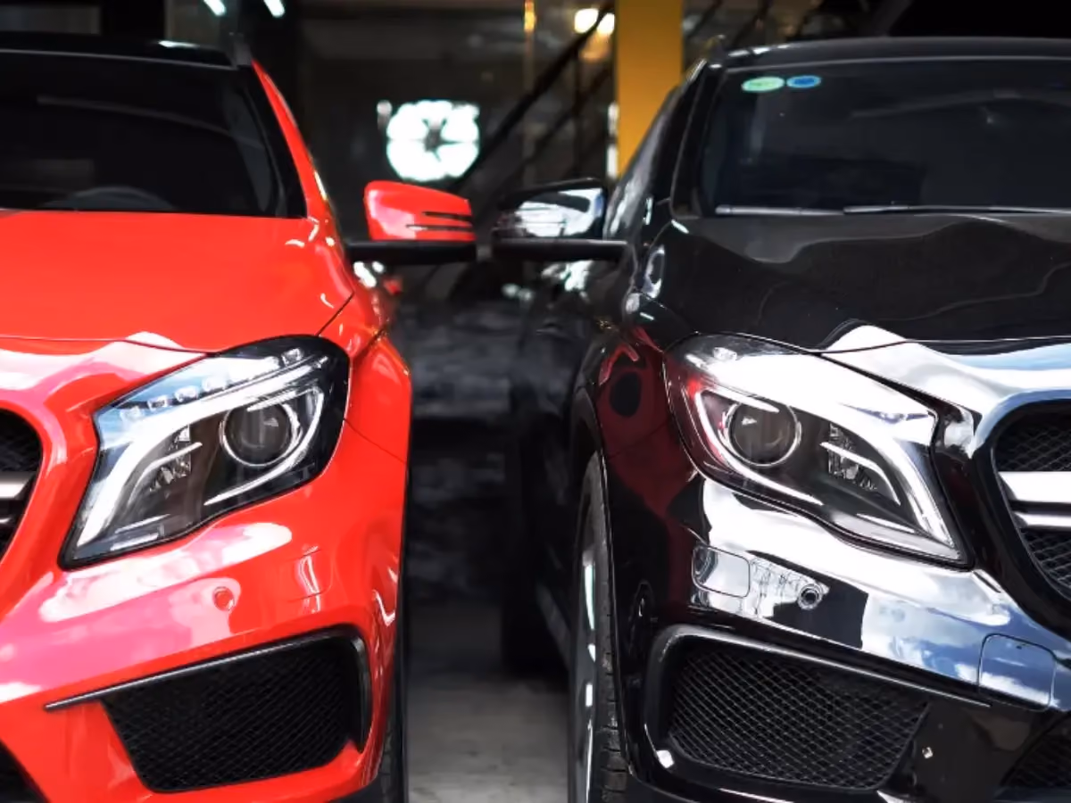 Close-up front view of a bright red car and a glossy black car parked side-by-side, showing their grilles and headlights.