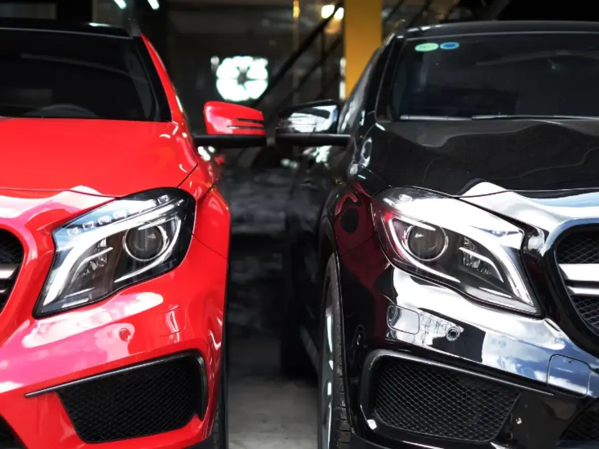 Close-up front view of a bright red car and a glossy black car parked side-by-side, showing their grilles and headlights.