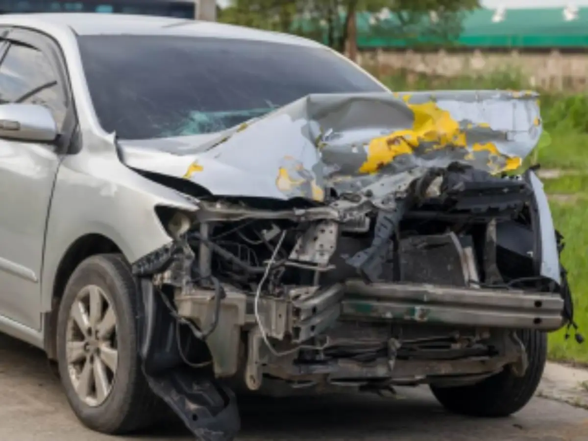 Silver sedan with severe front-end crash damage, showing a crumpled bonnet, smashed bumper, and exposed engine components.