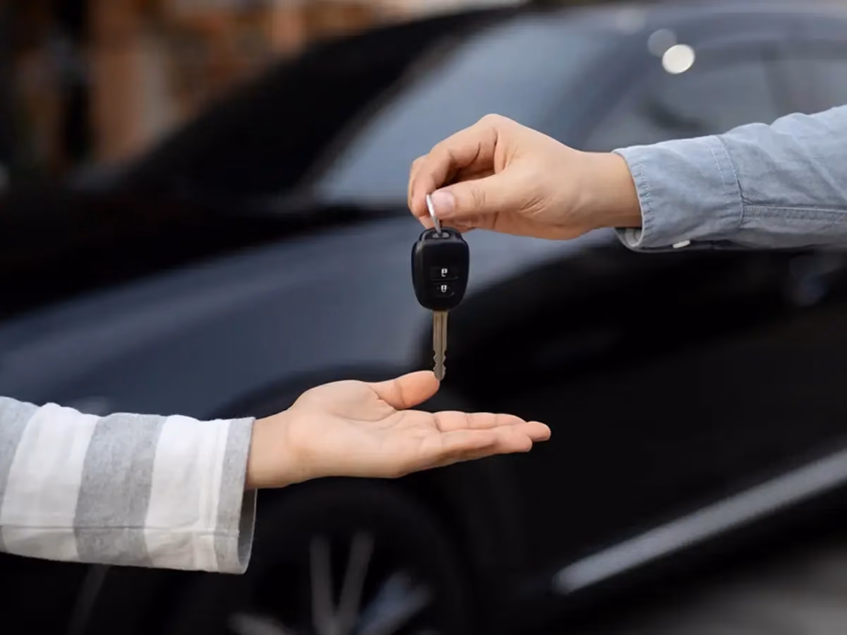 Close-up of a person handing over a black car key to another person's open palm in front of a sleek black vehicle.
