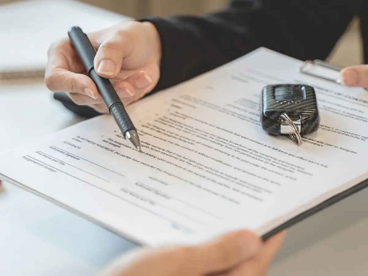 Close-up of a person holding a pen, about to sign a paper contract on a clipboard with a car key fob resting on top.