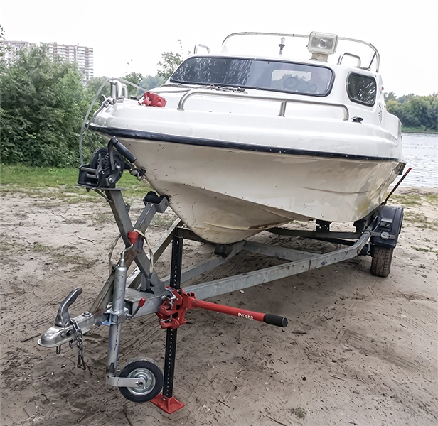 Used boat on trailer parked by a riverbank ready for transport.