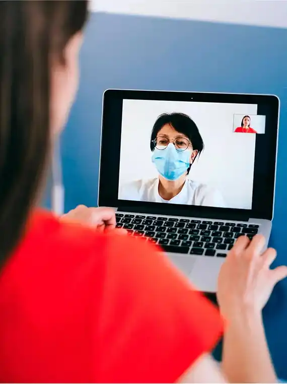 Eine Person hält einen Laptop hoch, auf dem eine Online-Videoberatung mit einer Zahnärztin zu sehen ist.