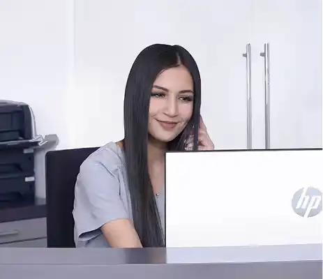 Eine lächelnde Frau sitzt am Schreibtisch und arbeitet an einem Laptop.