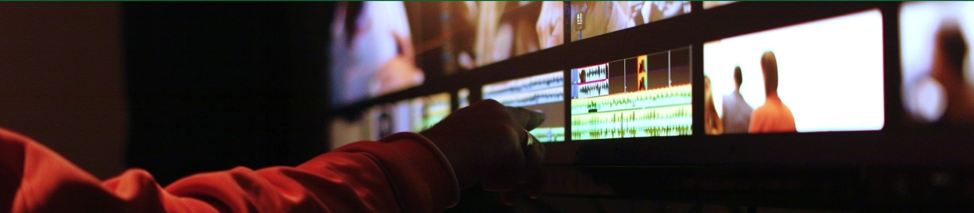 Person pointing at audio and video editing software on a computer screen in a dark room.