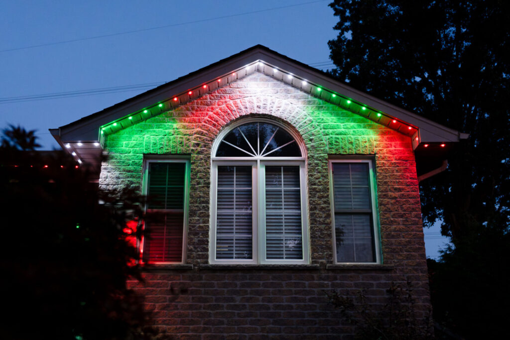 Red and green permanent Christmas lighting on a stone gable