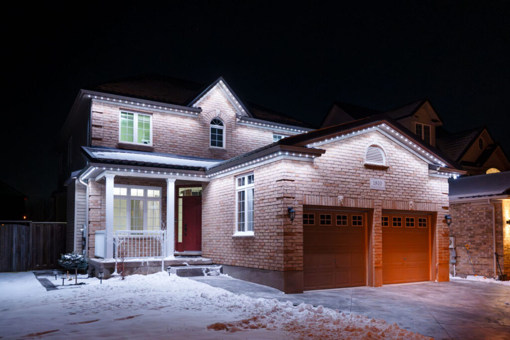 Warm white permanent lighting on a brick home in snow