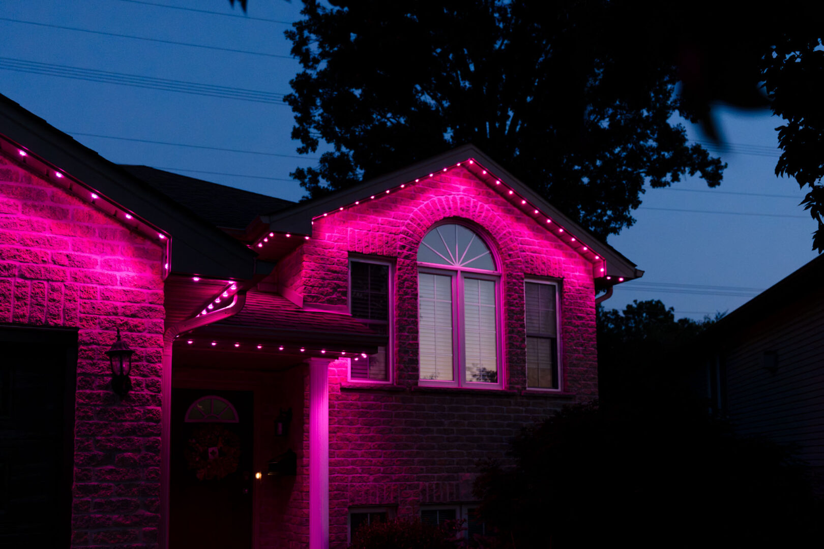 Magenta permanent lighting on a brick home with an arched window